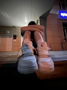 a person with their legs crossed sitting on the ground in front of a building at night