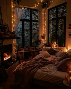 a bed with pillows and blankets in front of a window filled with lit candles next to a fire place