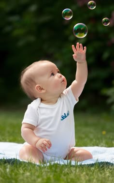 a baby sitting in the grass playing with soap bubbles