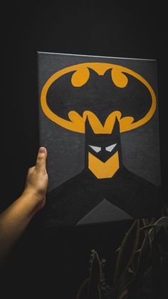 a hand holding up a batman poster in front of a black background with yellow lettering