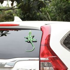 a lizard sticker on the back of a white car in front of some trees