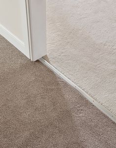 an open door on the side of a carpeted room with white walls and flooring