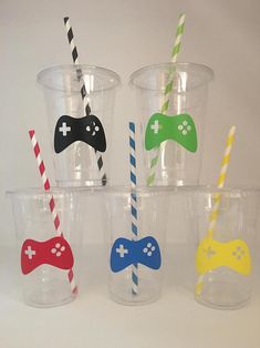 four plastic cups with different colored video game controllers on the lids and straws in each cup