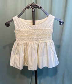 This is a sweet vintage, little girl's dress from the 50s or 60s. No labels or tags. About a size 2, the chest measures 22", please see measurements below.  Made of  butter yellow cotton in a pale yellow. It is sleeveless with a wide neckline. The bodice is smocked with yellow stitches. It has attached sashes at the side seam to tie in the back. The skirt is short & full & has a 4" hem.  Closes in the back with 2 small buttons.  The dress is in very good condition. No soil, stains. No damage or Cream Sleeveless Dress With Smocked Bodice, Sleeveless Smocked Bodice Cute Dress, Cute Sleeveless Smocked Dress For Spring, Cute Fitted Sleeveless Smocked Dress, Sleeveless Cotton Smocked Dress, Sleeveless Cotton Smocked Dress With Smocked Back, Cute Sleeveless Cotton Smocked Dress, Sleeveless Smocked Cotton Dress, Sleeveless Cotton Smocked Dress With Lining