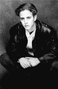 a black and white photo of a man in a leather jacket with his hands on his knees