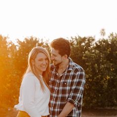 a man and woman standing next to each other in front of some bushes with the sun shining on them