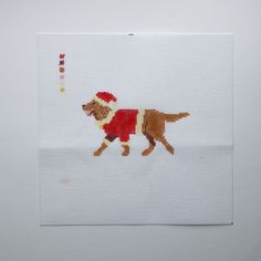 a cross - stitch picture of a dog wearing a santa hat and sweater, running with a toy in its mouth