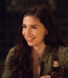 a woman sitting at a table with a beer in her hand and smiling for the camera