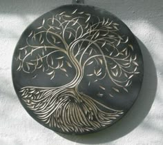 a metal plate with a tree on it hanging from a chain against a white wall