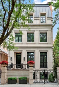 a two story house with black iron railings and red flowers on the front porch