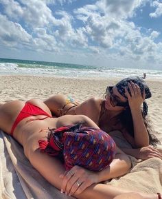 a woman laying on top of a sandy beach under a blue sky with white clouds