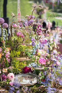 a birdcage filled with lots of flowers and greenery next to a metal tray