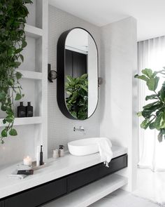 a white bathroom with black and white decor on the vanity, mirror and plants in pots