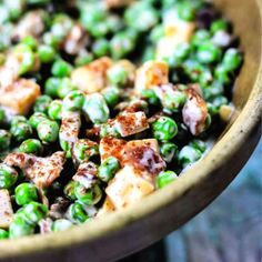 a wooden bowl filled with peas and tofu