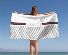 a woman is standing on the beach holding a gucci towel over her head while looking out at the ocean