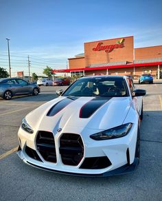 the front end of a white sports car parked in a parking lot next to a store