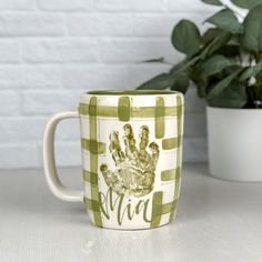 a coffee mug with a hand print on it next to a potted green plant