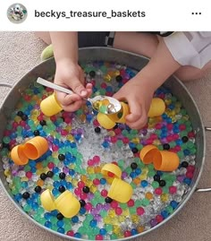 a child is playing with plastic cups in an ice bucket filled with water and gumballs