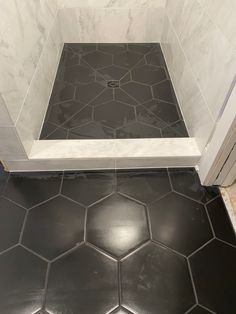 a black and white tiled bathroom with hexagonal floor tiles on the shower wall