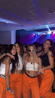 three women in orange pants are posing for the camera at a dance with their arms around each other