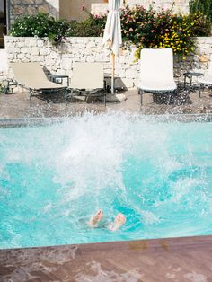 a person swimming in a pool with chairs and umbrellas around it on a sunny day