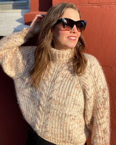 a woman wearing sunglasses standing next to a red wall with her hand on her head