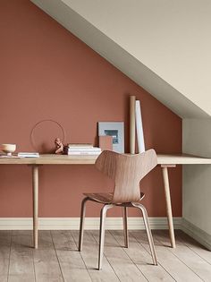 a desk with a chair and books on it in front of an orange painted wall