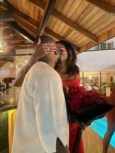 a man and woman standing next to each other in front of a swimming pool holding flowers