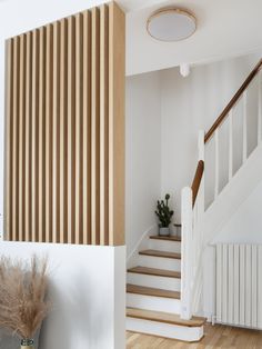 a white staircase with wooden slats on the wall and potted plant next to it