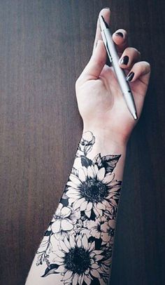 a woman's arm with flowers on it and a pen in the other hand