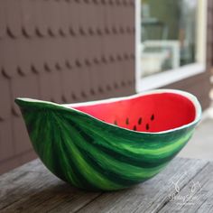 a red and green bowl sitting on top of a wooden table next to a building