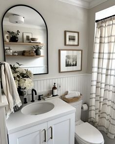 a white toilet sitting next to a sink in a bathroom under a mirror and framed pictures on the wall