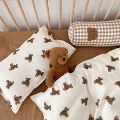 a brown teddy bear sitting on top of pillows next to a pillow case and crib