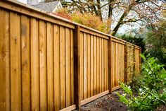 a wooden fence next to a lush green tree and shrubbery in front of a house