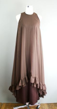 "This is a head-turner. It is a brown polyester sheath with a sheer chiffon overlay that features a high-low hemline. It is in excellent ready to wear condition. Estimated size S 34\" bust 28\" waist 38\" hip 54\" nape of neck to hem Purveyor's Note: We have searched far and wide, wrestled bears, braved the cold, traversed mountain ranges, fought pirates, swam with sharks and eaten at many a questionable road side taco stand to provide our customers with one of a kind vintage pieces. Know that w Beige Chiffon Party Dress With Ruffles, Beige Chiffon Dress With Ruffles For Party, Vintage Party Chiffon Dress, Sheer Chiffon Pre-draped Dress, Sheer Beige Chiffon Dress, Beige Sheer Chiffon Dress, Chic Brown Chiffon Dress, Flowy Silk Chiffon Dress For Cocktail, Flowy Silk Chiffon Dress