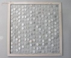 a painting with white dots on it hanging on the wall in front of a gray wall