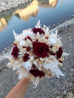 a bridal bouquet is held by someone's hand on the ground near water