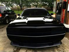 the front end of a black dodge charger parked next to a gas station pump