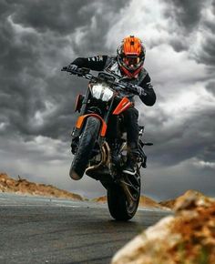 a man riding on the back of a motorcycle down a road under a cloudy sky