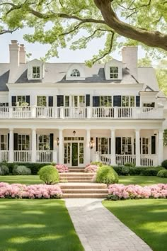 a large white house surrounded by lush green grass and pink hydrangeas in the front yard