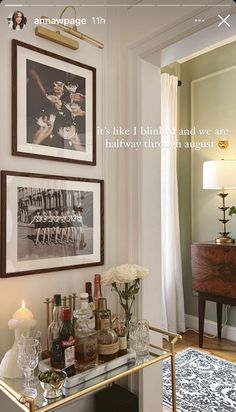 a bar cart with liquor bottles and glasses on it in front of two framed pictures