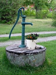 a green water faucet sitting on top of a wooden barrel filled with flowers