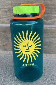 a blue mason jar with a yellow sun on the front and green lid, sitting next to a wooden fence