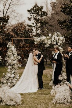 a bride and groom kissing under an arch of flowers at their wedding ceremony in the woods