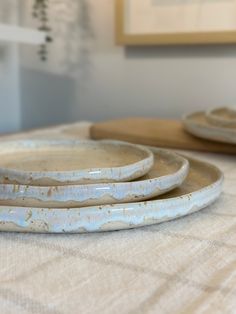 three white plates sitting on top of a table next to each other in front of a painting