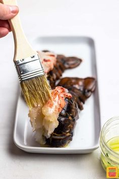 a person is holding a paint brush over some food on a white plate with sauce