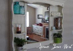 a mirror that is on the wall in front of a shelf with some potted plants