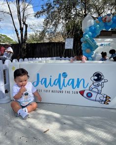 a baby sitting on the ground next to a sign