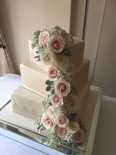 a three tiered wedding cake with pink and white flowers on the top, sitting on a table