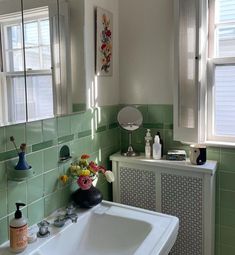 a bathroom with green tiles and white fixtures, including a large mirror above the sink